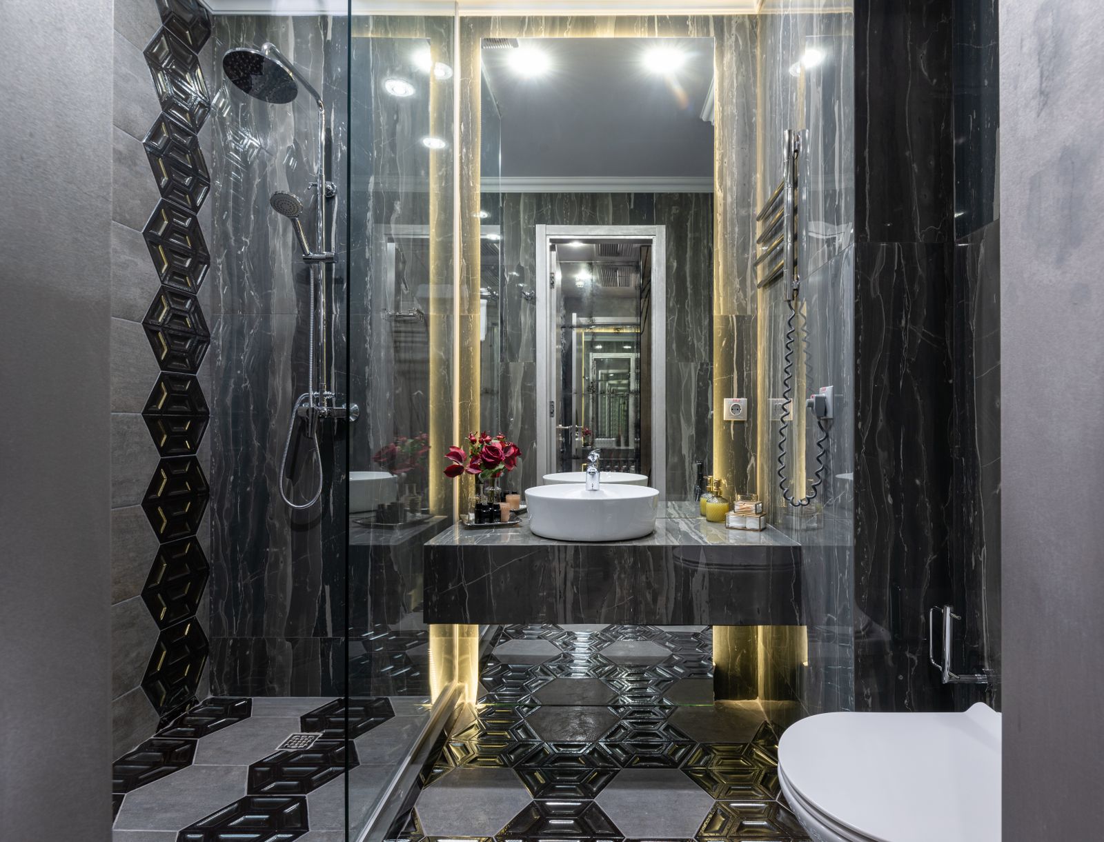 A contemporary bathroom with black tiled walls and a glass shower